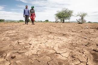 Zwei Menschen Hand in Hand auf ausgetrocknetem Boden. Dürre in Chimanimani (Bild: Karin Schermbrucker / Brot für die Welt)
